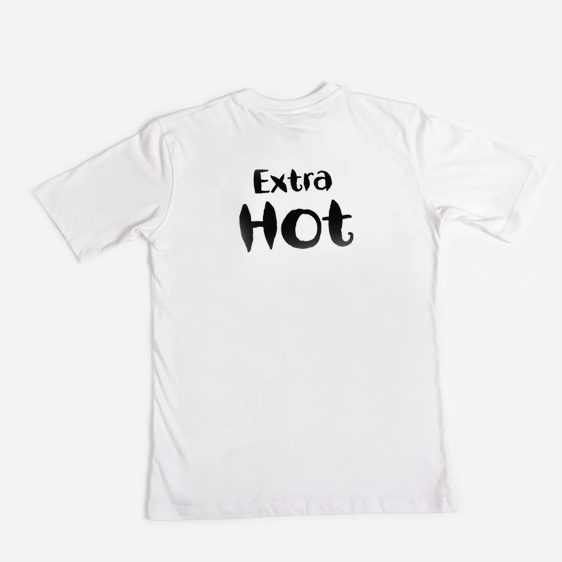 A white T-shirt with a small embroidered sauce bottle on the chest. Extra Hot is printed across the back in black.