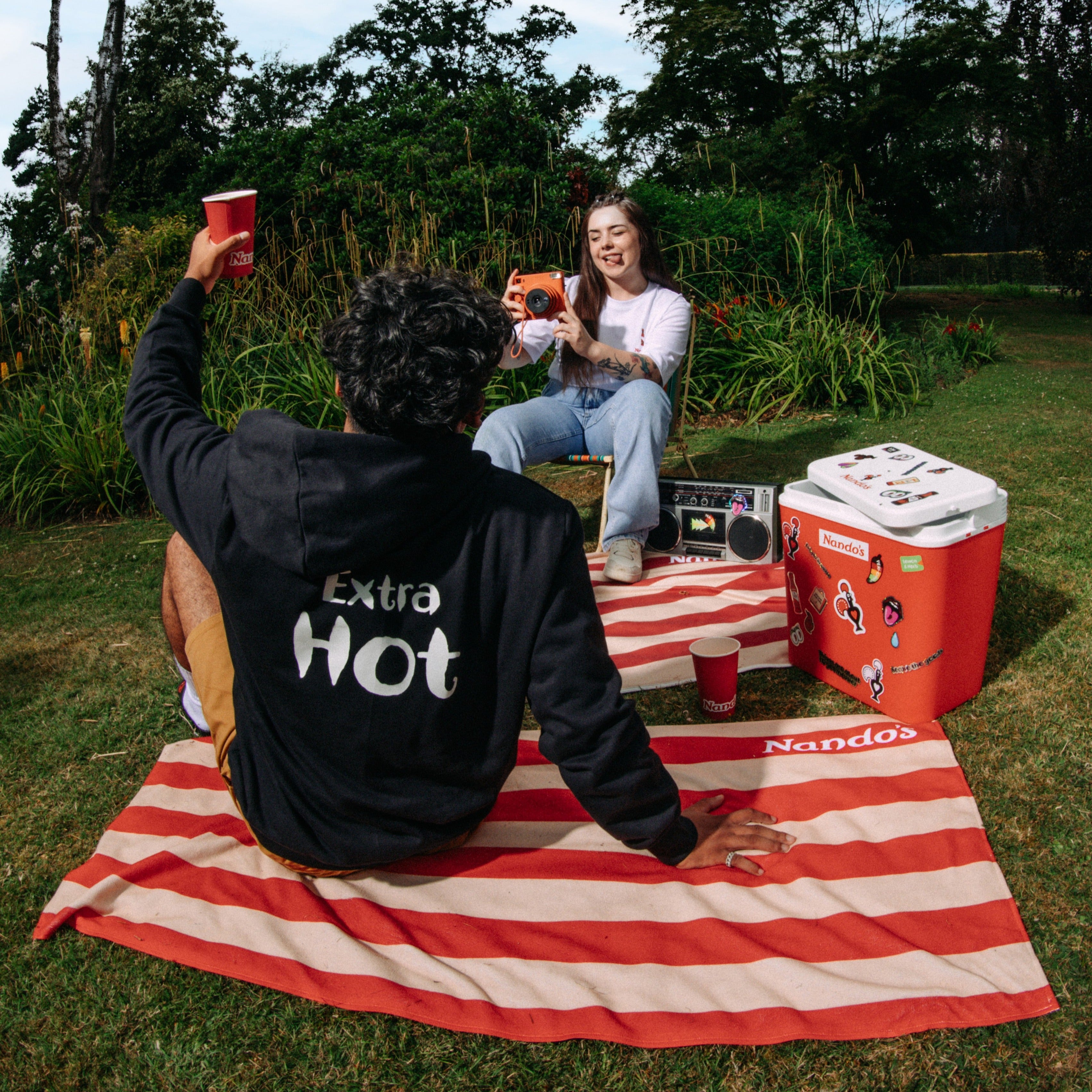 A black hoodie with a small embroidered sauce bottle on the chest. Extra Hot is printed across the back in white.